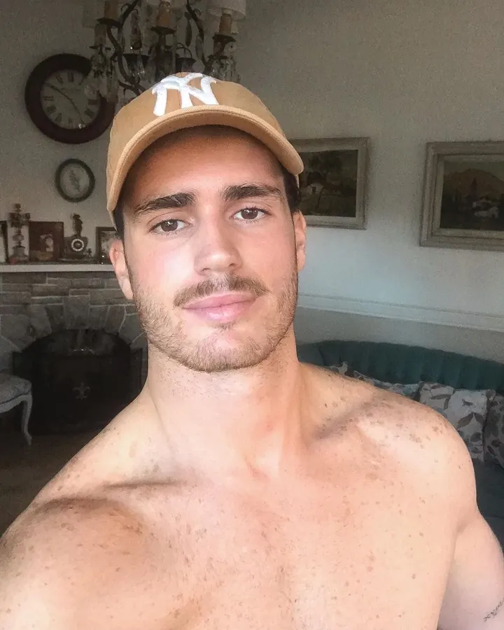 Homme européen portant une casquette beige avec logo blanc, torse nu, regard direct