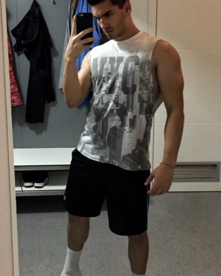 Homme barbu, regardant vers le côté, portant une chemise blanche légèrement ouverte, devant une fenêtre.