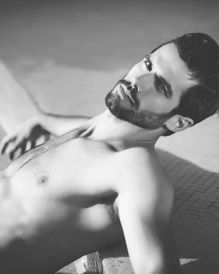 Homme européen de 25 à 35 ans, torse nu, portant un t-shirt blanc, sous-vêtement Calvin Klein, devant un rideau jaune.